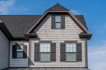 Gable with light shake shingle siding facade, double hung window, dark brown frame, on a Dutch pitched roof attic, American luxury single family colonial home neighborhood in USA blue sky, Alps style