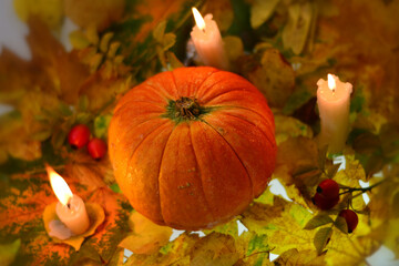 Orange halloween pumpkin on yellow autumn leaves with three burning candles