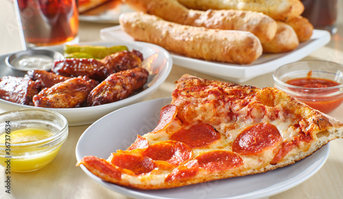 Cuadros en Lienzo sliced of pepperoni pizza on plate with breadsticks, soft drink and chicken wing