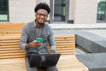 Wall Mural - young african man with laptop on bench, with mobile phone