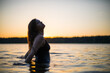 © Alexey Kartsev - Beautiful Russian girl in a long black swimsuit swims outside the city on the lake in the rays of sunset or dawn. Splashing water on the background of the sun. Happy girl.