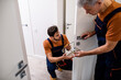 © Svitlana - Two locksmith, repairmen, workers in uniform installing, working with house door lock using screwdriver. Repair, door lock service concept