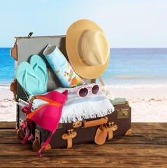 Wall Mural - Open vintage suitcase packed for summer vacation on wooden surface against sandy beach