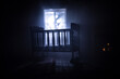 Old creepy eerie baby crib near window in dark room. Scary baby silhouette in dark. A realistic dollhouse living room with furniture and window at night