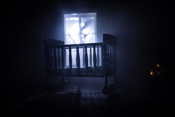 Wall Mural - Old creepy eerie baby crib near window in dark room. Scary baby silhouette in dark. A realistic dollhouse living room with furniture and window at night