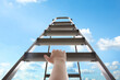 © New Africa - Woman climbing up stepladder against blue sky with clouds, closeup