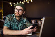 © mykolastock - Thoughtful modern handsome smart young bearded male hipster in hat using smartphone and laptop