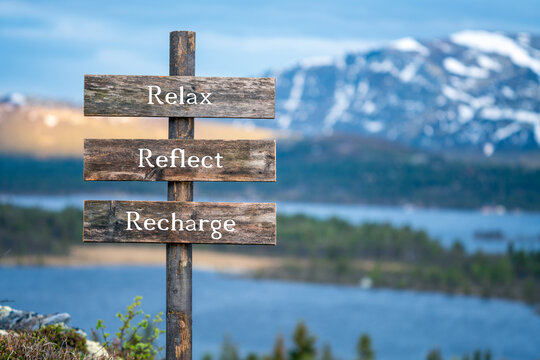 Wall Mural - relax reflect recharge text on wooden signpost outdoors in landscape scenery during blue hour. Sunset light, lake and snow capped mountains in the back.