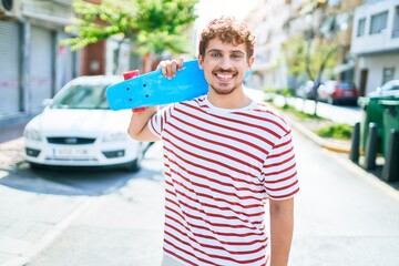 Young caucasian skater man smiling happy holding skate walking at street of city.