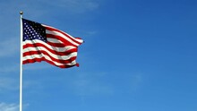American Flag Waving In The Wind In Slow Motion, With Vibrant Red White And Blue Colors Against Blue Sky, With Copy Space.