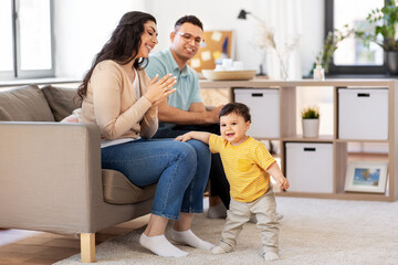 Wall Mural - family and people concept - happy mother, father and baby son sitting on sofa at home