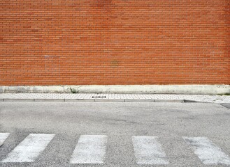 Wall Mural - Brick wall with a  sidewalk made of concrete tiles and a weathered  asphalt street with crosswalk. Background for copy space