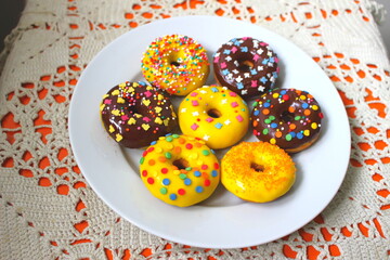 Assorted donuts on a plate. Rainbow dots decoration. Brown sugar. Lemon, melon, pineapple, mango, banana flavour. Chocolate