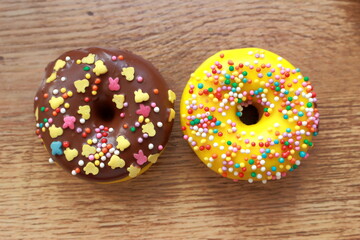 Assorted donuts on a wood background. Rainbow dots decoration. Brown sugar. Lemon, melon, pineapple, mango, banana flavour. Chocolate