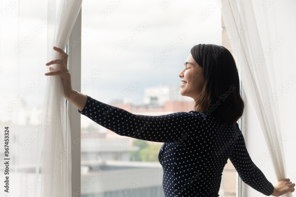 Overjoyed millennial Asian girl open curtains at home meet welcome new sunny early morning in own apartment or home, happy Vietnamese young woman smile for bright future, stress free concept - obrazy, fototapety, plakaty 