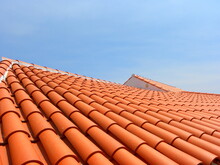 Red Tile Roof Under Blue Sky. The Photo Is Divided In Half. One Part Is A Roof Made Of Clay Tiles And The Other Is A Pure Blue Sky.