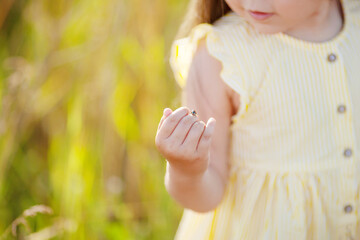 Cute little girl having ladybug on her hand. Close-up view of little girl wearing headband playing with ladybug in nature. Close up photo. Copy space