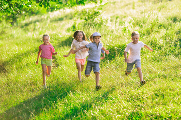 Wall Mural - Kids, children running on meadow in summer's sunlight. Look happy, cheerful with sincere bright emotions. Cute caucasian boys and girls. Concept of childhood, happiness, movement, family and summer.