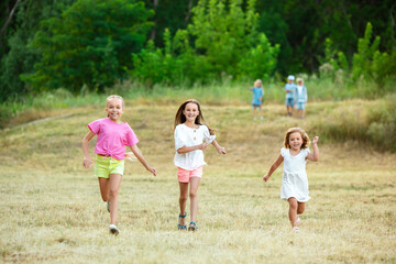 Wall Mural - Kids, children running on meadow in summer's sunlight. Look happy, cheerful with sincere bright emotions. Cute caucasian boys and girls. Concept of childhood, happiness, movement, family and summer.