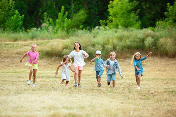 Wall Mural - Kids, children running on meadow in summer's sunlight. Look happy, cheerful with sincere bright emotions. Cute caucasian boys and girls. Concept of childhood, happiness, movement, family and summer.