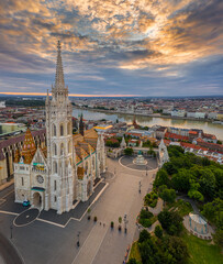 Wall Mural - Budapest, Hungary - Aerial drone view of the beautiful Matthias Church in the morning with Fisherman's Bastion (Halaszbastya) and Parliament of Hungary at background. Colorful clouds at sunrise