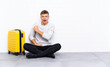 © luismolinero - Young handsome man sitting on the floor with a suitcase celebrating a victory