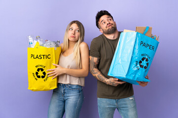 Poster - Young caucasian couple recycling isolated on purple background making doubts gesture while lifting the shoulders