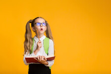 Surprised School Girl Learning Holding Book And Pencil, Yellow Background