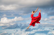 © Maria Moroz - young ballerina in a bright red long dress soars in a jump above the ground, like a bird, against a background of blue sky and clouds. The skirt develops like wings.