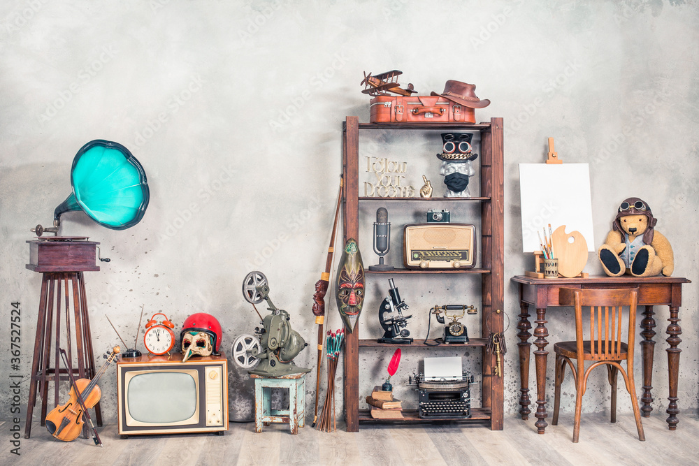 Collection of antique media devices, writers tools, gramophone, film projector, old Teddy Bear toy with canvas blank on easel, travel bag front concrete wall background. Vintage style filtered photo - obrazy, fototapety, plakaty 