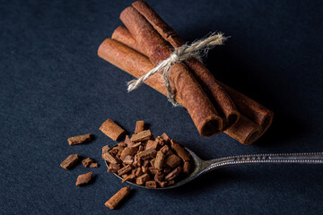 Cinnamon on a black background. spoon with crushed cinnamon. behind two sticks of cinnamon tied with a jute thread.