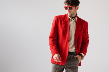 Wall Mural - fashionable man in red blazer and sunglasses holding hand in pocket isolated on grey