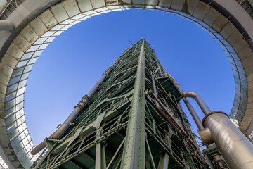 A bottom-up wide-angle view of an abandoned old refinery tower made of steel with its round ramp framing the image in a sunny day with a blue sky in Lisbon, Portugal.