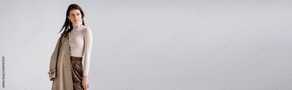 panoramic shot of fashionable woman holding trench coat and looking away isolated on grey - obrazy, fototapety, plakaty 