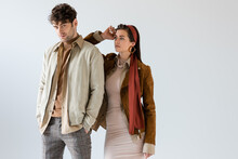 Trendy Girl In Autumn Outfit Posing Near Stylish Man With Hands In Pocket Isolated On Grey