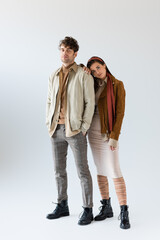 Wall Mural - Full length view of stylish woman in autumn outfit leaning on man standing with hands in pockets on grey