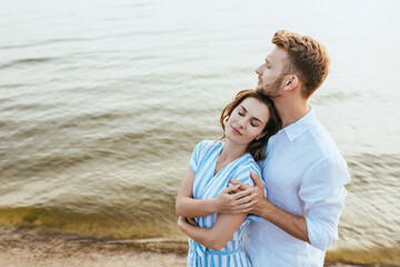 bearded man hugging beautiful girlfriend near river