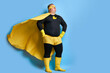 handsome brave strong man has a mad desire, a dream to shield the world from dirt and evil. fat superhero in yellow costume posing isolated over blue background