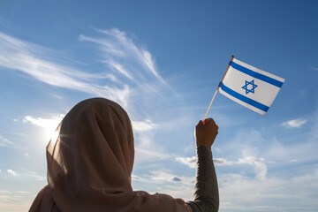 Wall Mural - Silhouette of muslim woman in head scarf with Israel flag at blue sunset sky. Concept of freedom