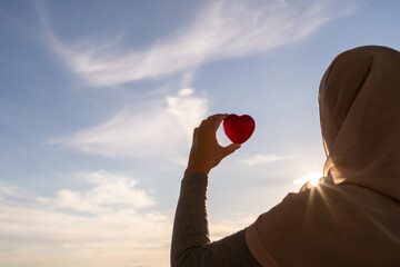 Poster - Silhouette of muslim woman in head scarf with red heart on blue sunset sky background. Concept