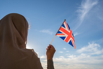 Wall Mural - Silhouette of muslim woman in head scarf with Great Britain flag at blue sunset sky. Concept of freedom