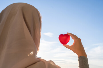 Poster - Silhouette of muslim woman in head scarf with red heart on blue sunset sky background. Concept