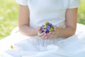 A girl's hands full of wildflowers dressed for religious communion.