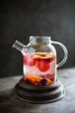 Fototapeta Kwiaty - Fruit tea in a large transparent teapot. Warm lemonade with fruits and berries. Dark photo. Minimalism. Beautiful dishes.