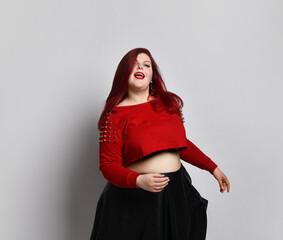 Wall Mural - Obese ginger lady in red spiked top, black bra and leather skirt. She is dancing, posing isolated on white photo background