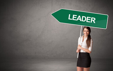 Young business person in casual holding road sign with LEADER inscription, new business direction concept