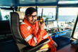 © Igor Kardasov - Filipino deck Officer on bridge of vessel or ship wearing coverall during navigaton watch at sea . He is speaking on portable GMDSS VHF radio, short range communication