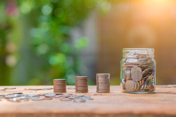 Saving money by hand puting coins in jug glass on nature background