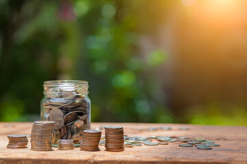 Saving money by hand puting coins in jug glass on nature background