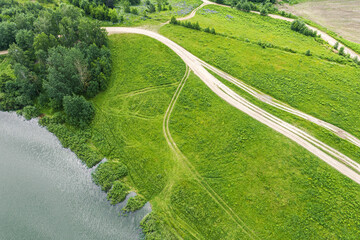 Wall Mural - countryside landscape in summer. rural dirt road on green meadow near lake. birds eyes view